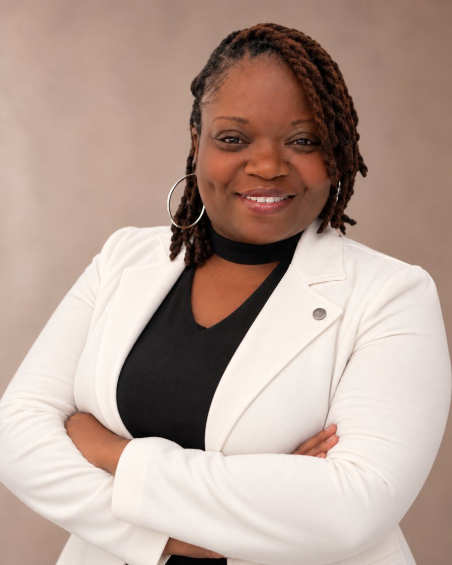Author Lisa E. Dean smiling with her arms crossed, wearing a white blazer over a black top.